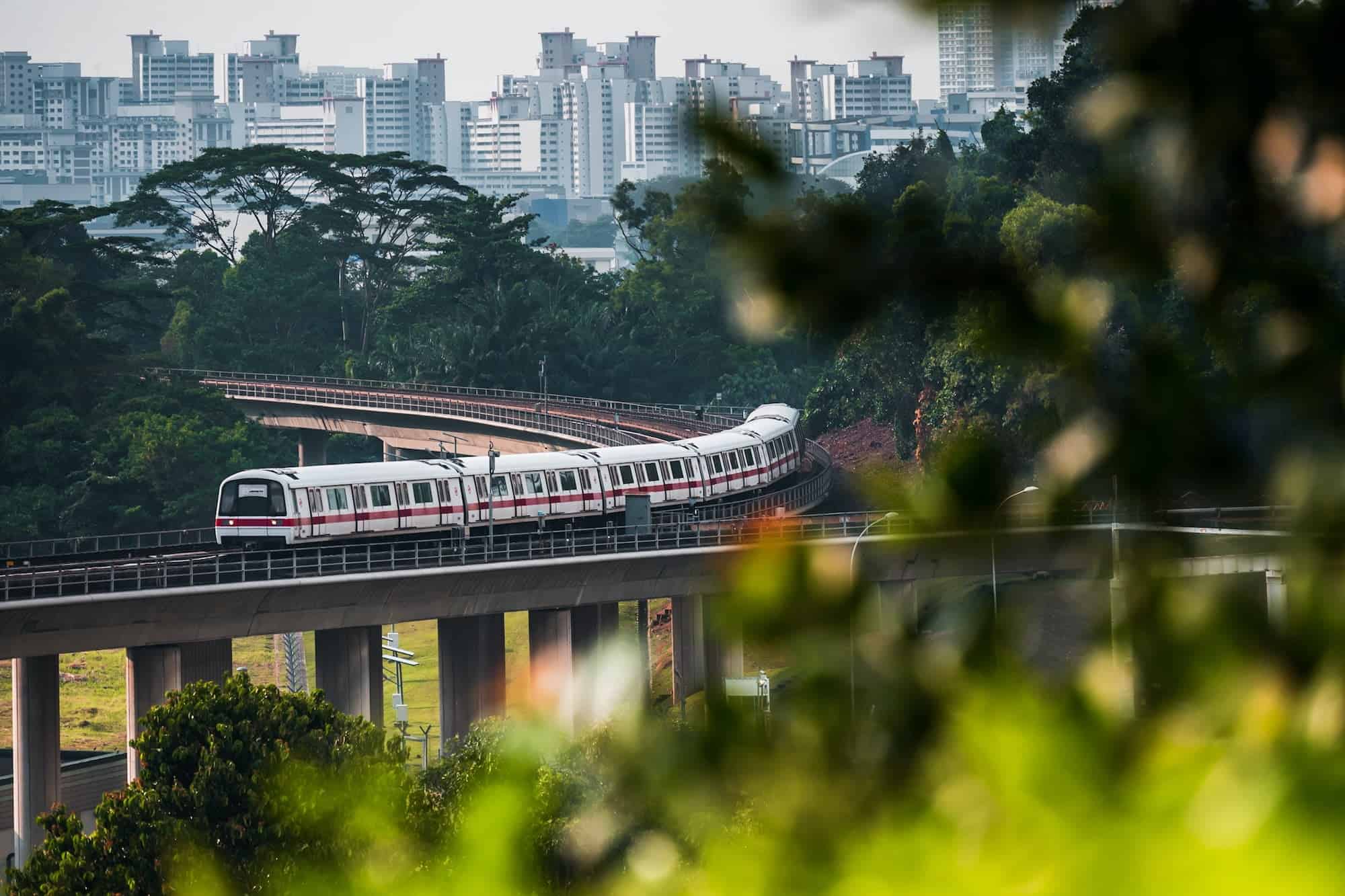 A Mass Rapid Transit (MRT) train making its way around a bend through the landscape of lush greenery